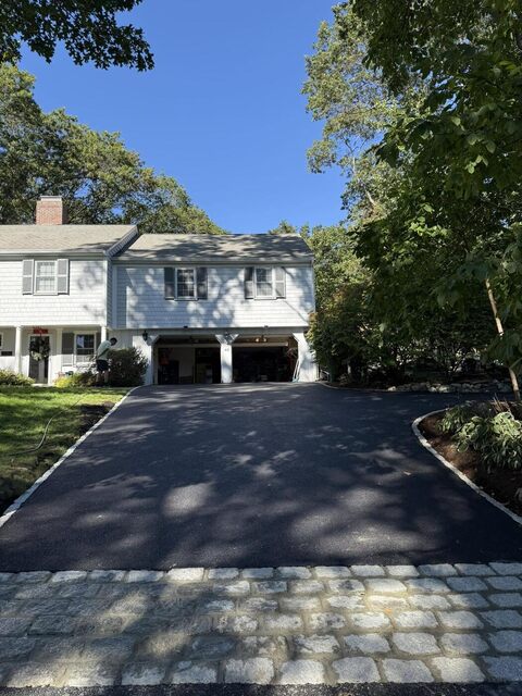 New asphalt driveway with a granite cobblestone apron at the street and cobblestone edging along the planting beds, leading to a two-car garage.